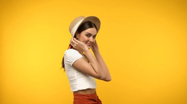 Hasır şapkalı güzel bir kadın sarıya izole edilmiş kameraya bakıyor. 
