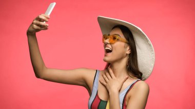 Mayo giymiş heyecanlı bir kadın cep telefonundan selfie çekiyor. Pembe renkte. 