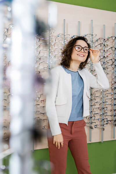happy woman trying on eyeglasses in optics store on blurred foreground