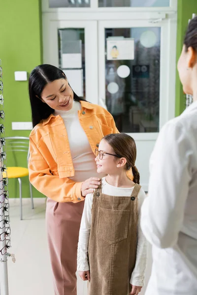 Asian Woman Talking Smiling Daughter Blurred Ophthalmologist Optics Store — Zdjęcie stockowe