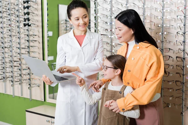 Smiling Girl Eyeglasses Pointing Laptop Oculist Asian Mom Optics Store — Stockfoto