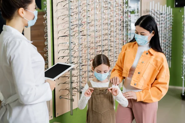 Girl Medical Mask Choosing Eyeglasses Asian Mother Blurred Oculist Digital — Foto de Stock