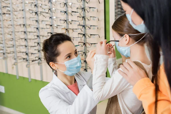 光学商店里戴着医用口罩的眼科医生在近视亚洲女人时试戴女用眼镜 — 图库照片