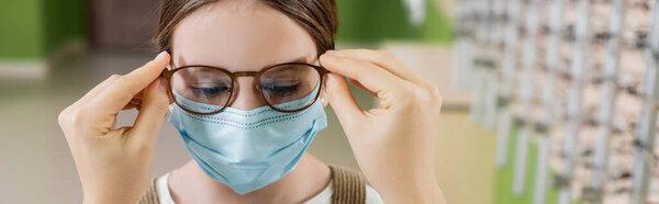 oculist putting eyeglasses on girl in medical mask, banner