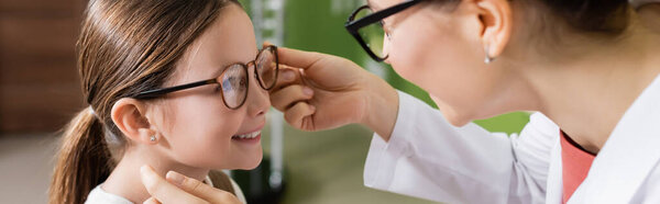 ophthalmologist trying eyeglasses on smiling girl in optics store, banner