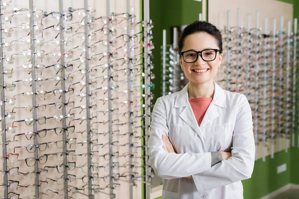 Pleased Ophthalmologist White Coat Eyeglasses Standing Crossed Arms Optics Store — Fotografia de Stock