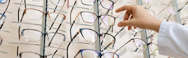 cropped view of oculist taking eyeglasses in optics store, banner