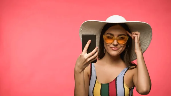 Smiling Woman Swimsuit Sunglasses Holding Smartphone Pointing Head Isolated Pink — стоковое фото