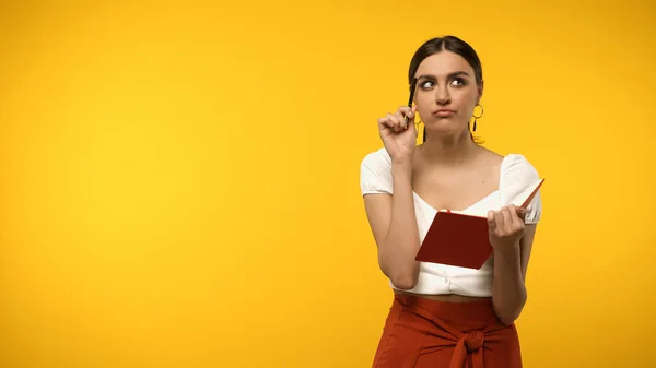 Thoughtful Woman Holding Pen Notebook While Standing Isolated Yellow — Foto de Stock