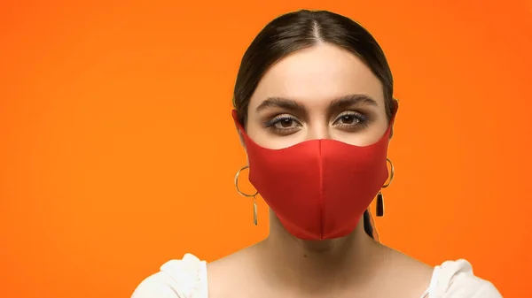 Young Woman Protective Mask Earrings Looking Camera Isolated Orange — стоковое фото