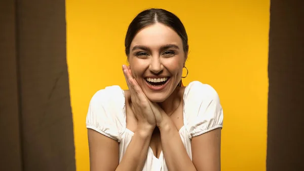 Bottom view of positive woman in blouse looking at blurred box isolated on yellow