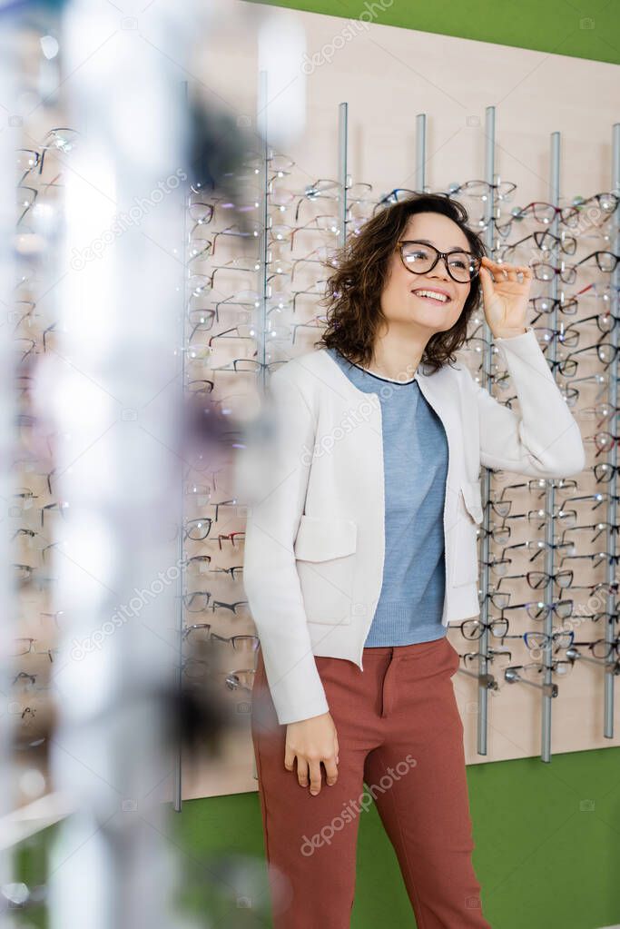 happy woman trying on eyeglasses in optics store on blurred foreground