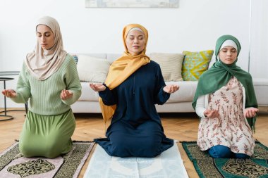 Multiethnic women and teenager praying with closed eyes at home  clipart