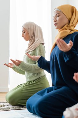 Asian mother and young muslim daughter praying at home  clipart