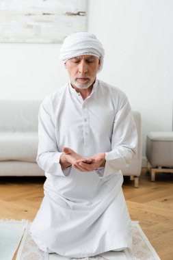 Geleneksel Müslüman kıyafetleri içinde evde dua eden olgun bir adam. 