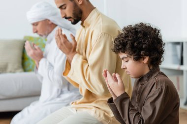 Kıvırcık Müslüman çocuğun evde ırklar arası ebeveynlerin yanında dua edişinin yan görüntüsü 