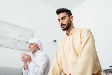 Olgun bir babanın yanında dua eden sakallı bir Arap 'ın düşük açılı görüntüsü. 