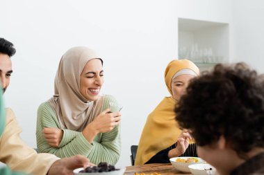 tesettürlü neşeli Müslüman kadın yemek boyunca çok kültürlü bir aileyle gülüyor.