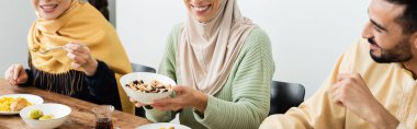 smiling woman holding bowl with nuts during dinner with muslim family, banner clipart