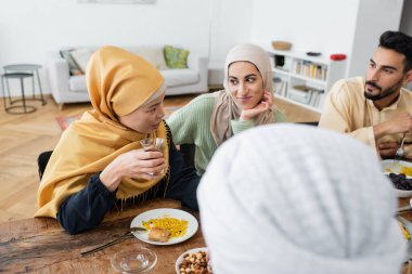 Orta yaşlı Asyalı kadın evde yemek yerken Müslüman ailesiyle konuşuyor.