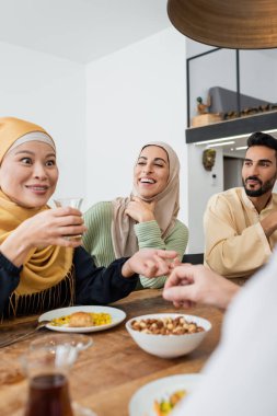 Mutlu Müslüman bir ailenin yanında çay içen heyecanlı Asyalı kadın.