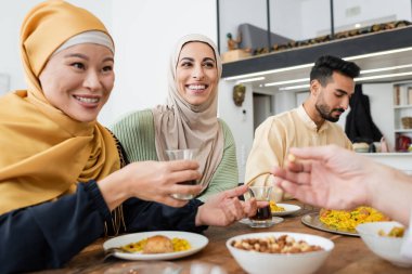 Müslüman ailesiyle yemek yerken elinde çay tutan neşeli Asyalı kadın.