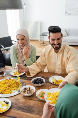 Neşeli Müslüman kadın evde ailesiyle yemek yerken gülüyor.