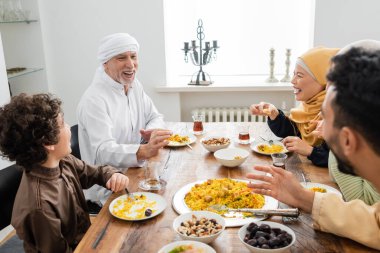 Mutlu orta yaşlı Müslüman adam evde yemek yerken ırklar arası aileyle konuşuyor.
