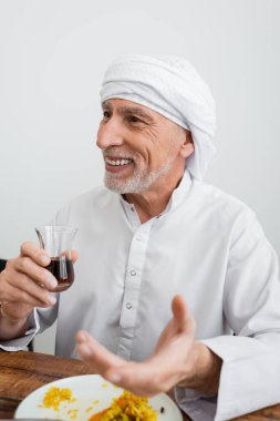 Türbanlı mutlu Müslüman adam tabakta pilav yanında bir bardak çay tutuyor.