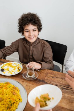 happy muslim arabian boy smiling during dinner with blurred family clipart