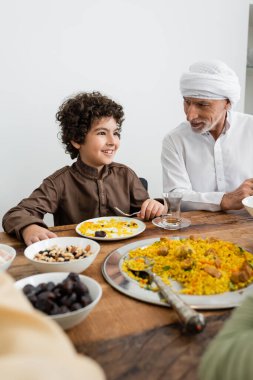 Gülümseyen Arap çocuk aile yemeği yiyor. Müslüman büyükbabanın yanında.