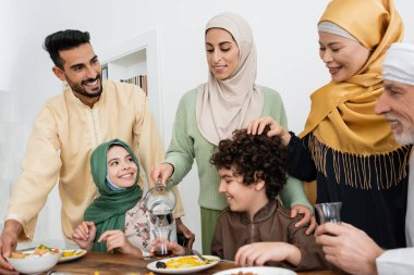 Neşe dolu Arap kadın, ırklar arası Müslüman ailesiyle yemek yerken çay içiyor.