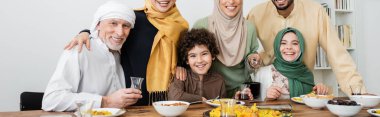 Çok ırklı Müslüman aile pilav yakınında kameraya gülümsüyor ve masada çay, pankart