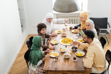 high angle view of happy multiethnic muslim family having dinner at home clipart