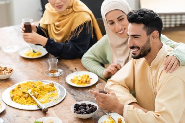 Masanın yanında kocasını kucaklayan neşeli Müslüman kadın aile yemeğiyle servis ediliyor.