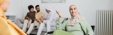 Mutlu Müslüman kadın bulanık annesiyle konuşuyor. Evde ırklar arası bir ailenin yanında, pankartta.