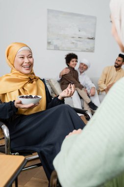 tesettürlü mutlu Asyalı kadın, bulanık kızı ve çok ırklı Müslüman ailesinin yanında hurma tutuyor.