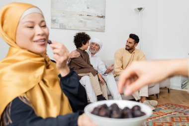 Bulanık Asyalı kadın elinde kaseyle oturma odasında ırklar arası Müslüman bir ailenin yanında duruyor.