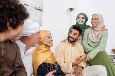 Gülümseyen Arap adam, neşeli çok ırklı Müslüman ailesiyle konuşurken elini işaret ediyor. 