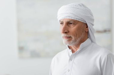 Beyaz sarıklı orta yaşlı bir adam evine bakıyor.