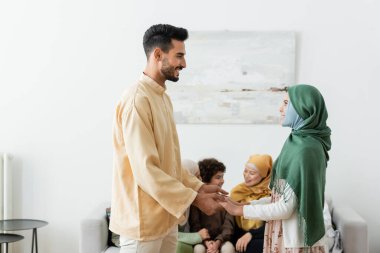 Bulanık arka planda, çok ırklı Müslüman bir ailenin yanında kızıyla el ele tutuşan mutlu bir Arap adam.