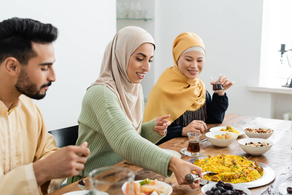 muslim woman serving pilaf near asian mother and blurred husband