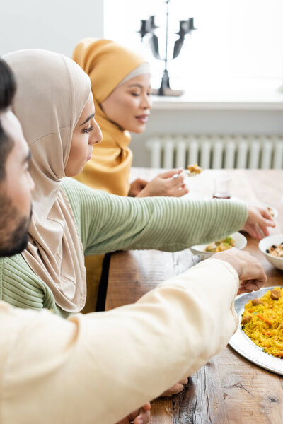 young muslim woman having dinner with blurred multiethnic family