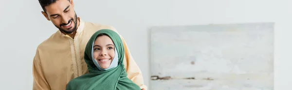 穿着头巾的穆斯林女孩在家里靠近阿拉伯父亲微笑 高举横幅 — 图库照片