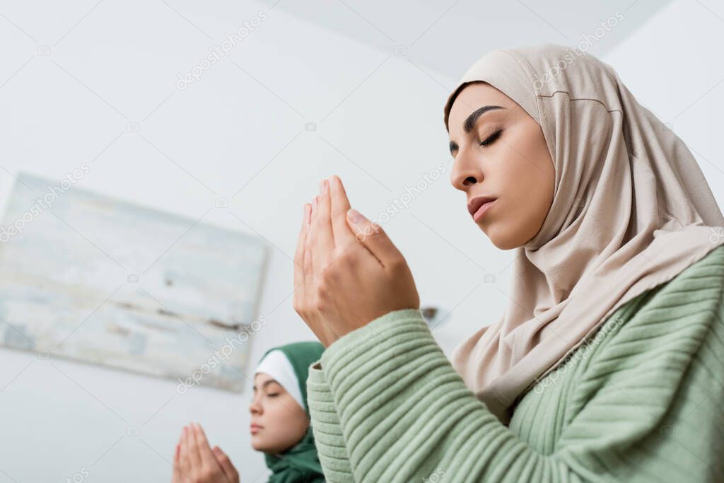 Low angle view of arabian woman praying near blurred daughter at home 