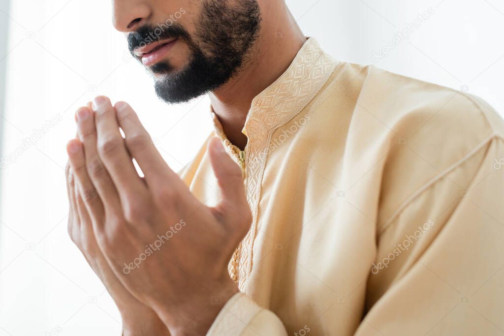 Cropped view of young bearded muslim man praying at home 