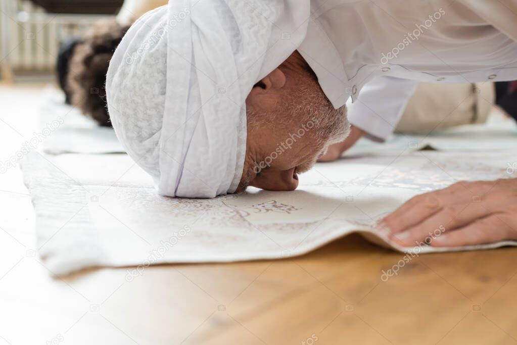 Side view of middle aged man praying on blurred rug at home 