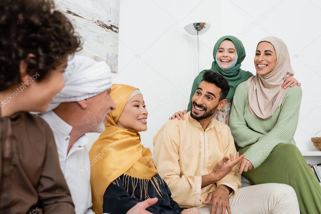 smiling arabian man pointing with hand while talking to cheerful multiethnic muslim family 