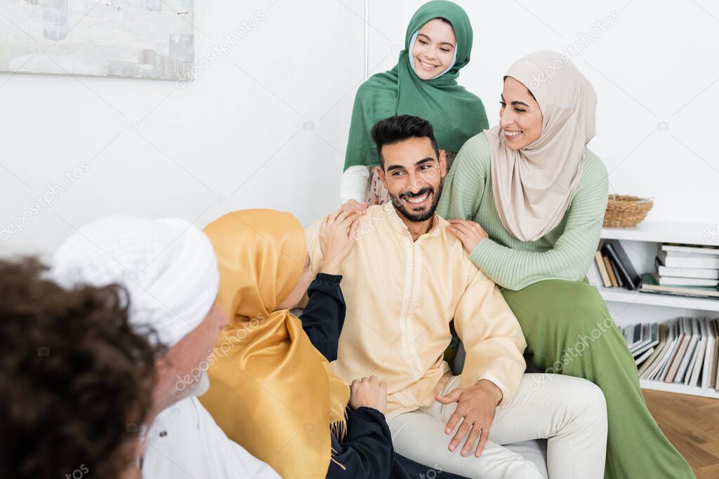 arabian man smiling near multicultural muslim family on sofa at home