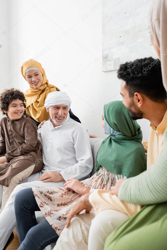 smiling muslim man talking to granddaughter near multicultural family